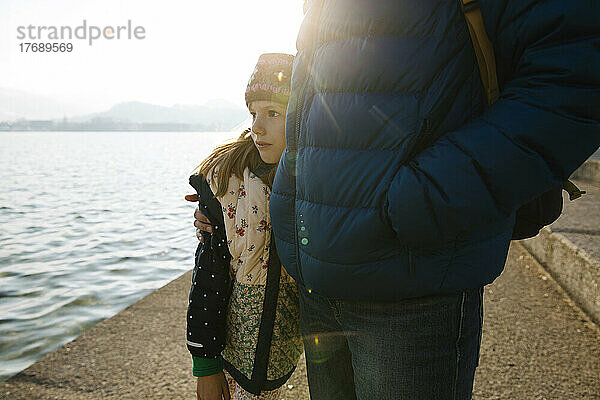 Mädchen steht an sonnigem Tag mit Vater am See