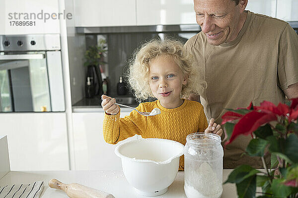 Glückliches blondes Mädchen  das zu Hause vom Vater in der Küche gebacken wird