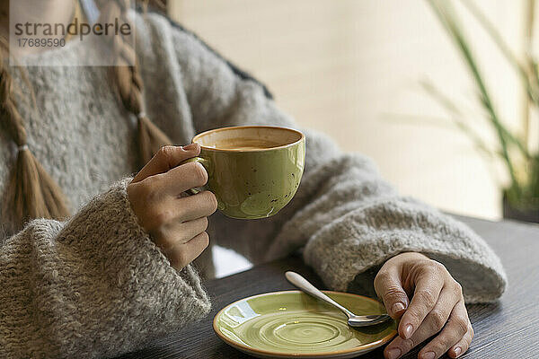 Junge Frau mit Kaffeetasse sitzt im Café