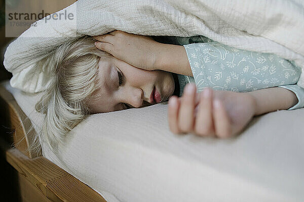 Girl sleeping under blanket on bed at home