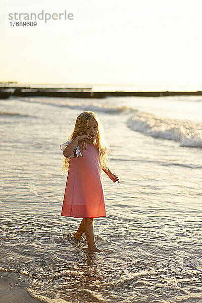 Nettes Mädchen mit blonden Haaren  das am Strand spaziert