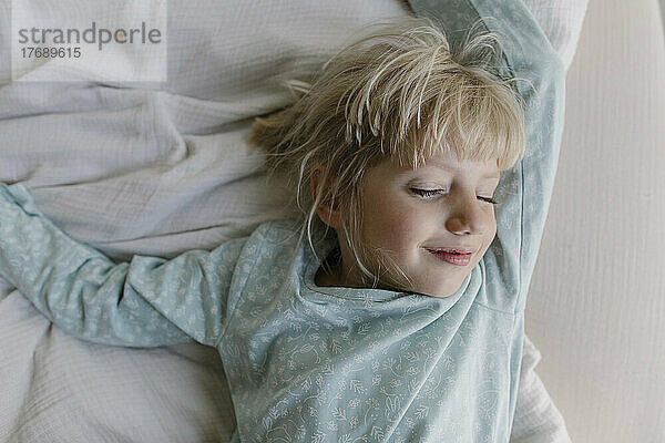 Smiling girl with eyes closed lying on bed at home