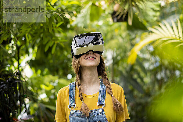 Lächelnde Frau mit Virtual-Reality-Simulator steht im Garten