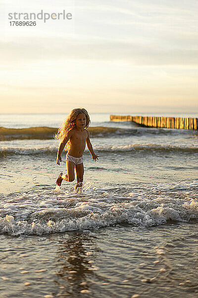 Nettes Mädchen in Unterwäsche  das am Strand im Wasser spielt