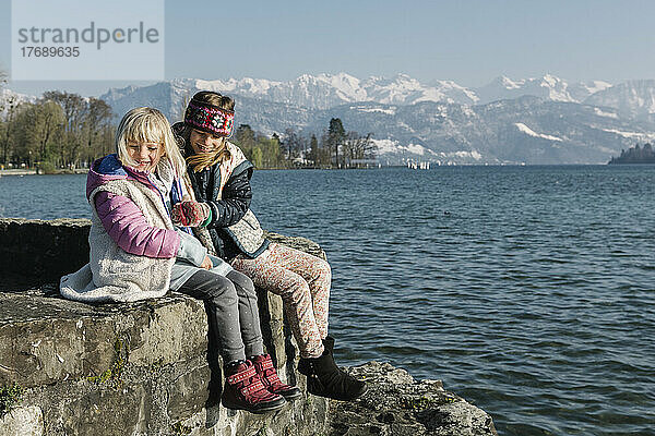 Glückliche Schwestern sitzen auf der Mauer am See