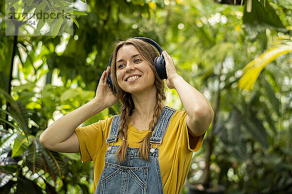 Lächelnde Frau hört im Garten Musik über kabellose Kopfhörer