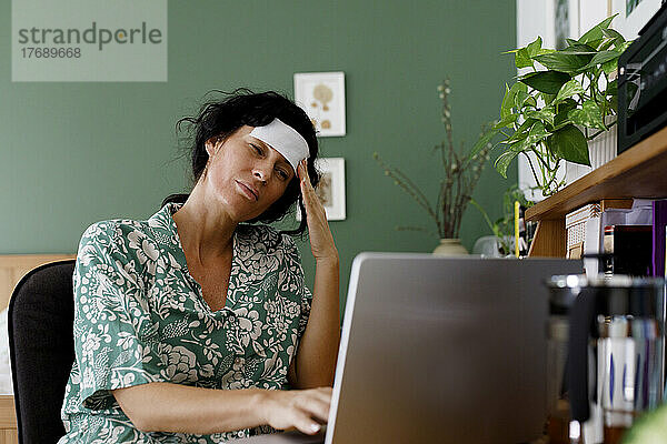 Überarbeitete Geschäftsfrau  die zu Hause am Laptop unter Kopfschmerzen leidet