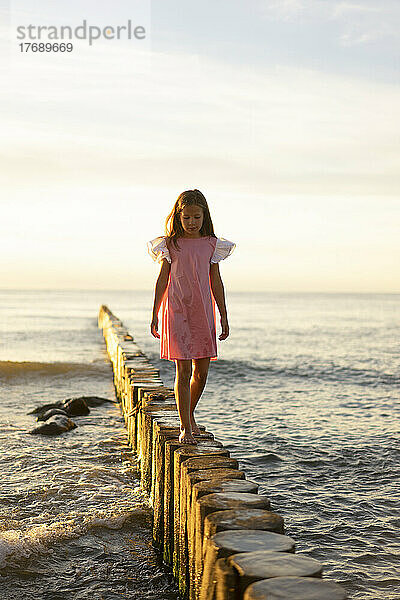 Mädchen läuft auf Holzpfosten am Strand