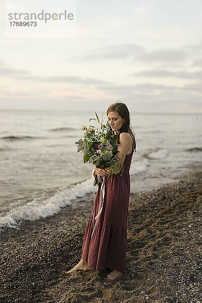 Frau hält Blumenstrauß am Strand