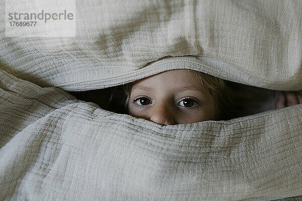 Girl peeking out from blanket at home