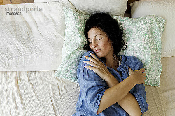 Woman lying in bed hugging herself at home