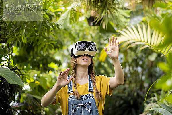 Junge Frau mit Virtual-Reality-Simulator gestikuliert im Garten