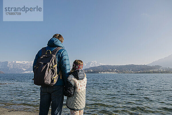 Vater trägt Rucksack und steht mit Tochter am See