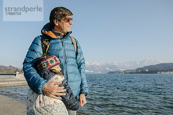 Glücklicher Vater mit Sonnenbrille steht an einem sonnigen Tag mit seiner Tochter am See