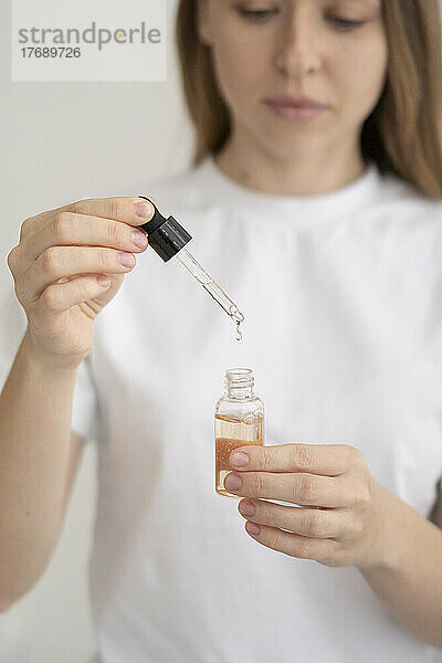 Young woman pouring drop in essential oil bottle