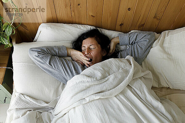Frau mit geschlossenen Augen gähnt zu Hause im Bett