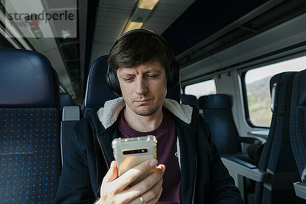 Mann mit Kopfhörern und Smartphone sitzt auf Sitz im Zug