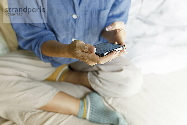 Hände einer Frau mit Mobiltelefon  die auf dem Bett sitzt