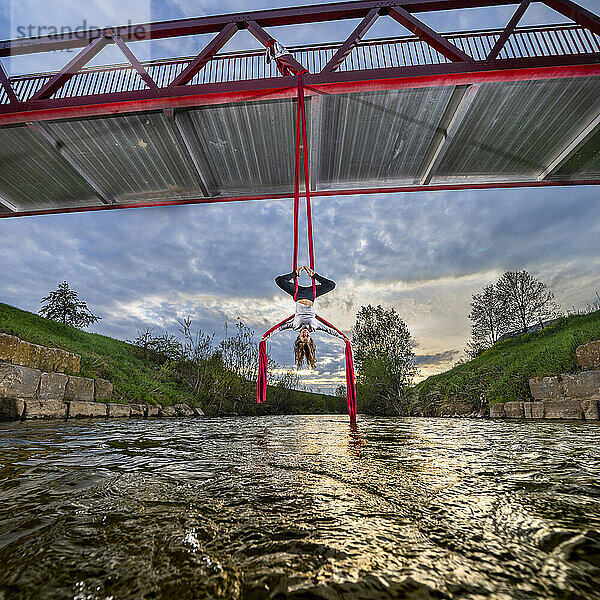 Sportler übt kopfüber hängend Luftakrobatik an der Brücke über den Fluss Rems