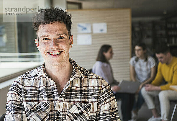 Lächelnder junger Geschäftsmann im Büro mit Kollegen im Hintergrund
