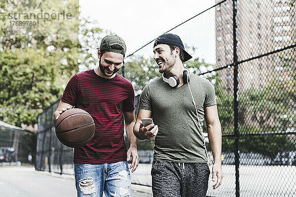 Zwei lächelnde Freunde mit Basketball im Freien