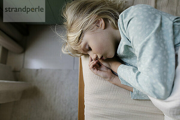 Girl with blond hair sleeping on edge of bed at home