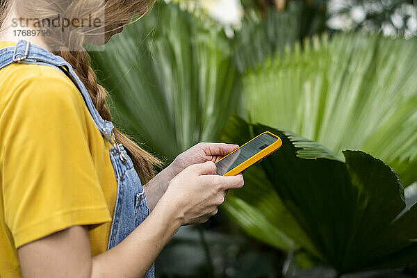 Junge Frau mit braunen Haaren benutzt Smartphone im Garten
