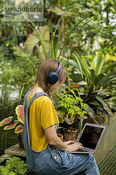 Junge Frau benutzt Laptop und hört Musik über kabellose Kopfhörer im Garten