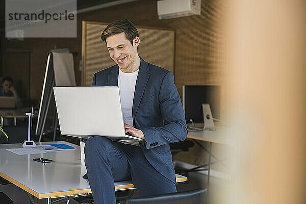 Lächelnder Geschäftsmann mit Laptop im Büro