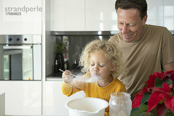 Smiling man looking at daughter blowing flour in kitchen