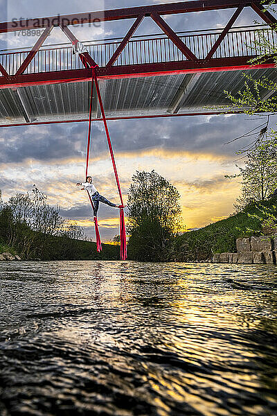 Sportler üben Luftakrobatik  hängend von der Brücke über den Fluss Rems bei Sonnenuntergang
