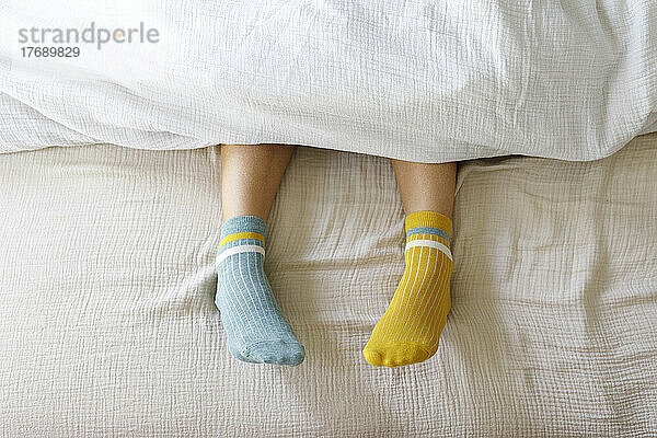 Woman wearing blue and yellow socks in bed at home