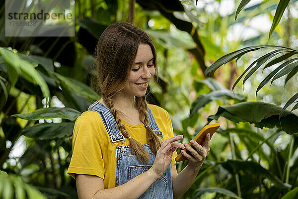 Lächelnde junge Frau benutzt Smartphone im Garten