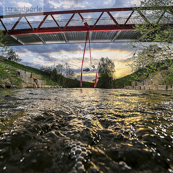 Sportler üben Luftakrobatik  hängend von der Brücke über den Fluss Rems