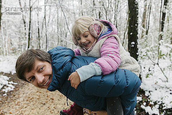 Vater huckepack mit Tochter im Winterwald