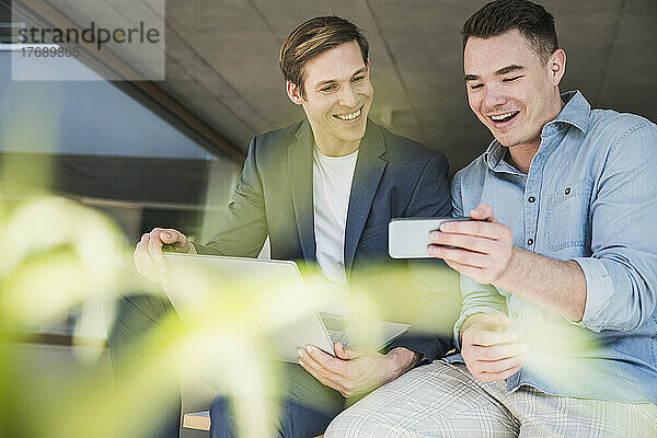 Zwei glückliche Kollegen teilen sich ihr Smartphone im Büro