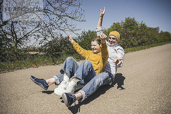 Glücklicher älterer Mann  der an einem sonnigen Tag mit seiner Enkelin Skateboard fährt