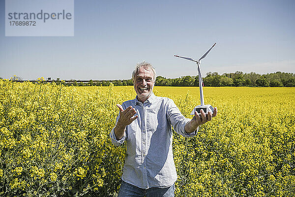 Glücklicher Mann mit Modell einer Windkraftanlage  der an einem sonnigen Tag in der Ablage steht