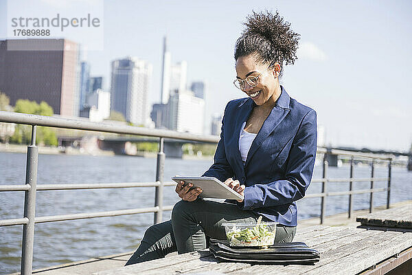 Glückliche Geschäftsfrau mit Tablet-PC auf Bank sitzend