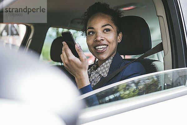 Glückliche Geschäftsfrau mit Mobiltelefon im Auto