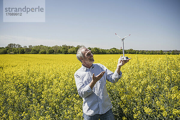 Glücklicher älterer Mann hält ein Modell einer Windkraftanlage  die auf dem Feld steht