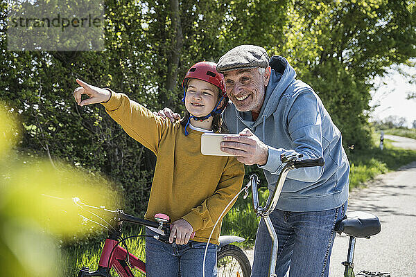 Glücklicher älterer Mann mit Mobiltelefon und Enkelin  die wegzeigt