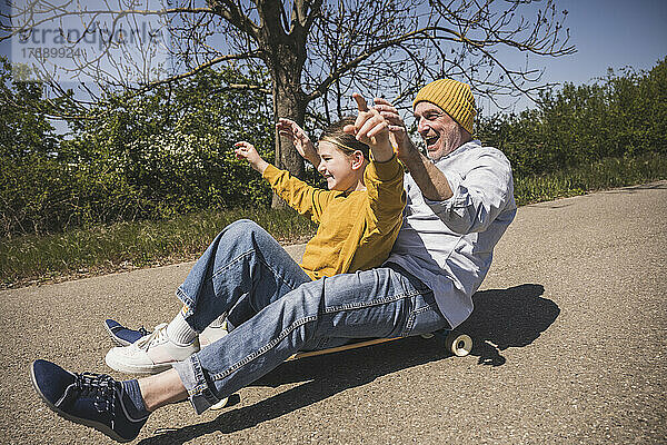 Fröhlicher älterer Mann genießt Skateboardfahren mit Enkelin auf der Straße