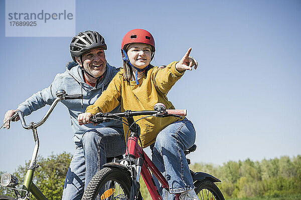 Lächelnder Großvater und Enkelin gestikulieren auf dem Fahrrad sitzend