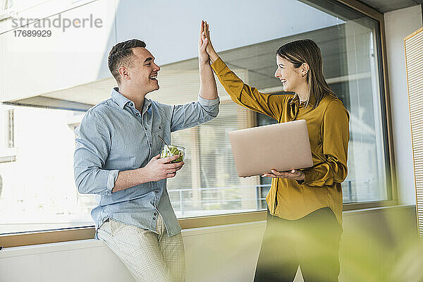 Geschäftsmann und Geschäftsfrau mit Laptop-High-Five am Fenster im Büro