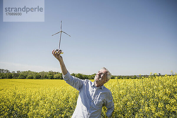 Lächelnder Mann blickt auf das Modell einer Windkraftanlage  die im Feld steht