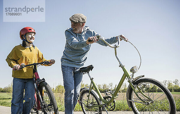 Lächelnder Großvater und Enkelin mit Fahrrad an sonnigem Tag
