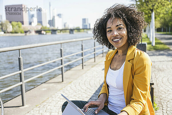 Lächelnde Geschäftsfrau mit Laptop am Main an einem sonnigen Tag