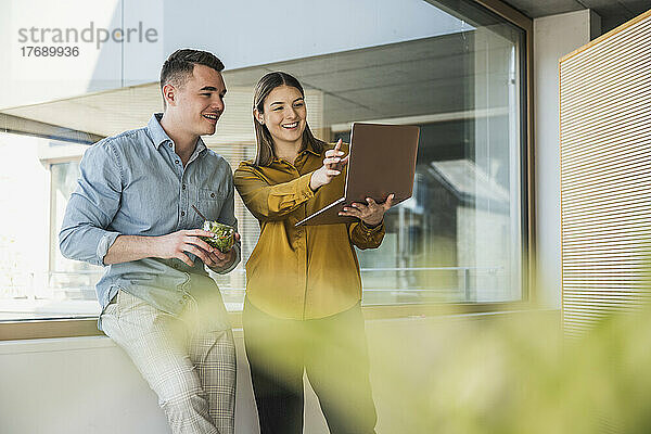 Geschäftsmann und Geschäftsfrau mit Laptop und gesundem Mittagessen am Fenster im Büro