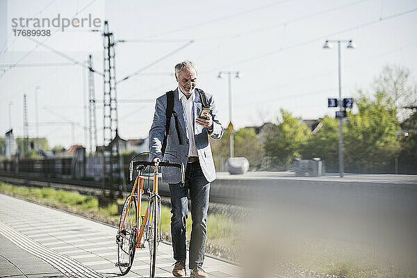 Geschäftsmann benutzt Smartphone und läuft mit Fahrrad auf Bahnsteig